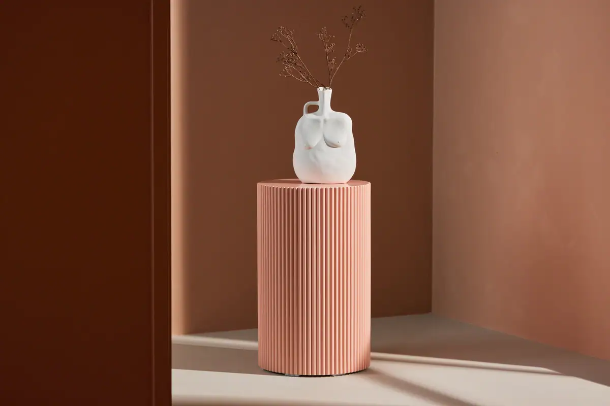 Snygg vit vas med konstnärlig design på rosa, ribbad piedestal – perfekt för avkoppling.