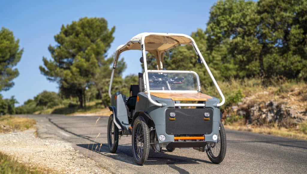 Le vélomobile Bob de Sanka Cycle circulant sur une route de campagne ensoleillée, entouré d'arbres méditerranéens.