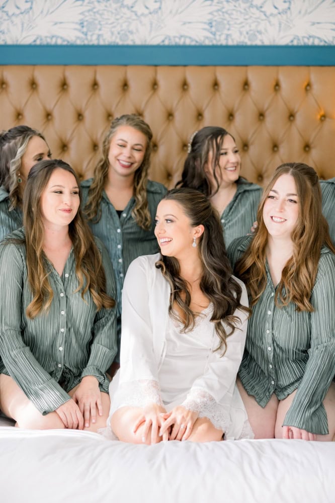 Bride and her friends laughing at each other while sitting on a hotel room bed