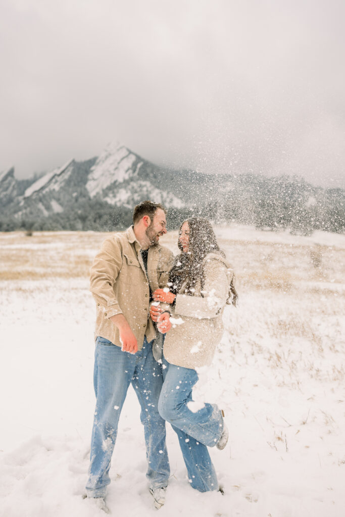 Couple playfully throwing snow in the air during their engagement session at Chautauqua Park in Boulder Colorado