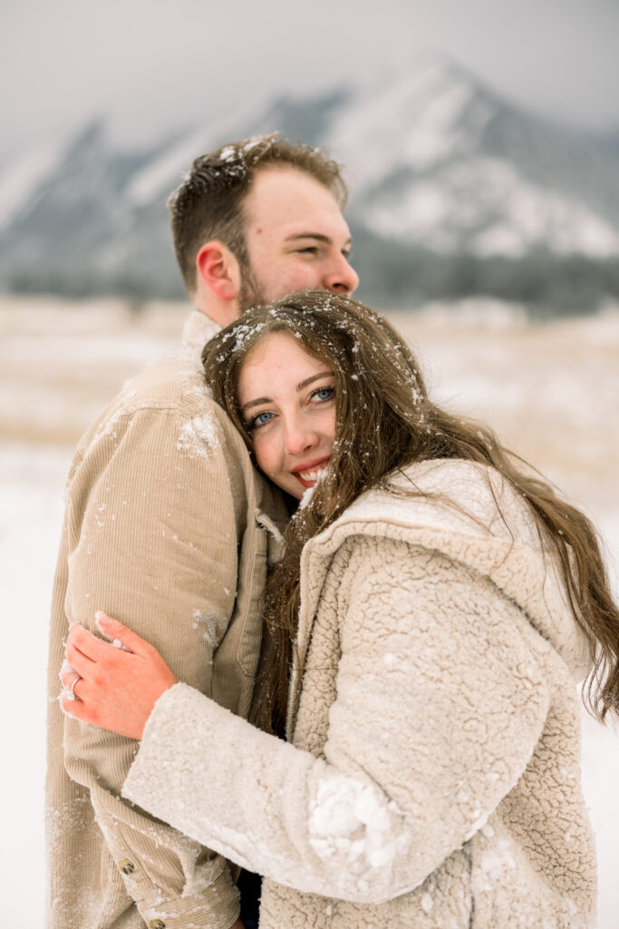 Couple cuddling into each other covered in snow
