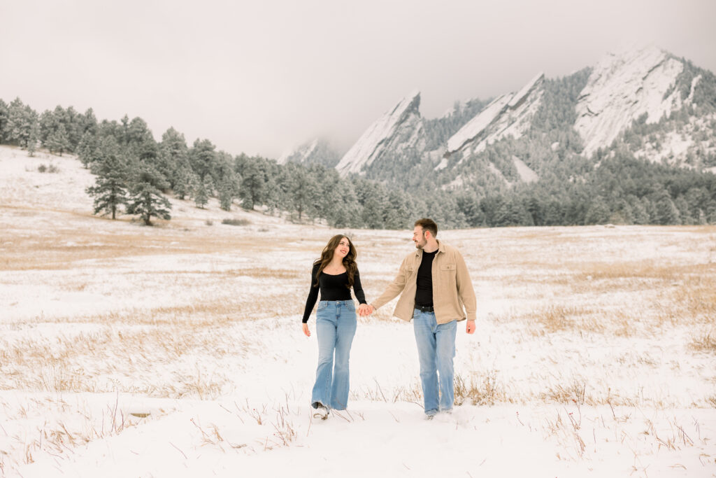 Couple holding hands walking while smiling at each other during engagement session at Chautauqua Park in Boulder Colorado