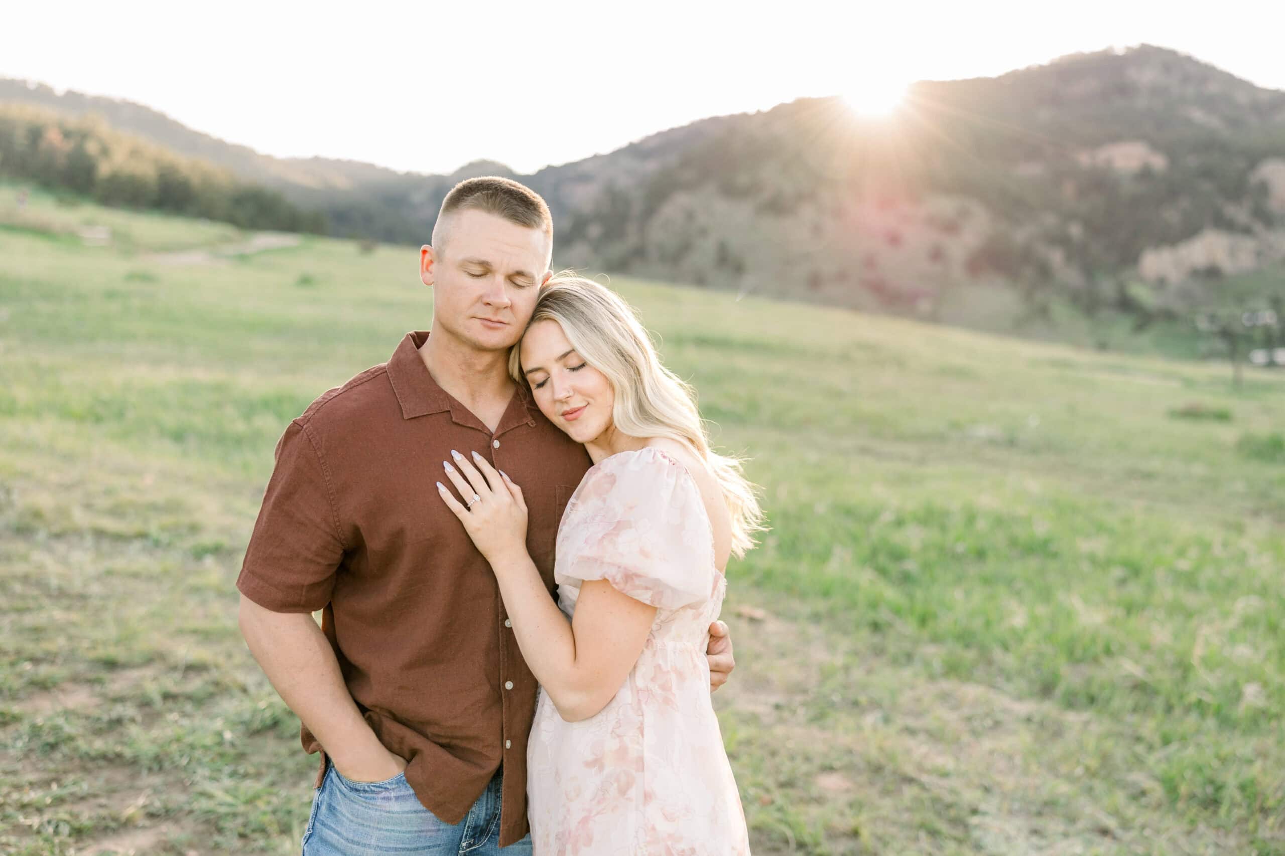 Couple cuddling into each other during golden hour as sun dips behind the mountains