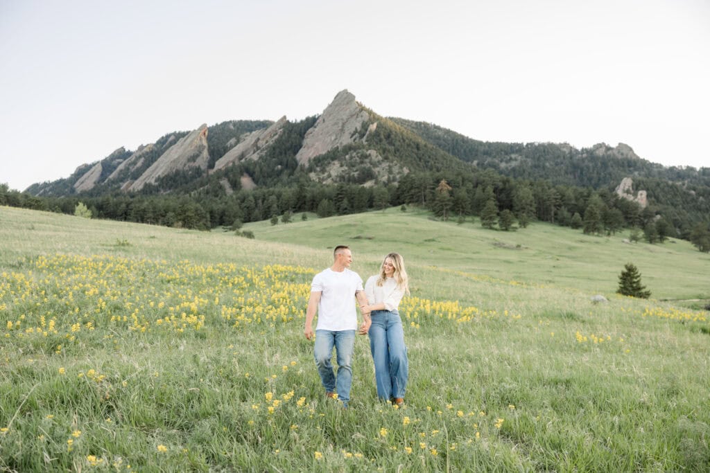 Couple walking through field with the Boulder Flatirons in the background
