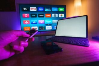 a hand holding a remote control next to a laptop