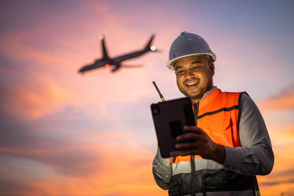 Smart engineer wearing safety uniform working with tablet near airport at night. Maintenance Engineer using tablet to checking inspection in night lights of industry background