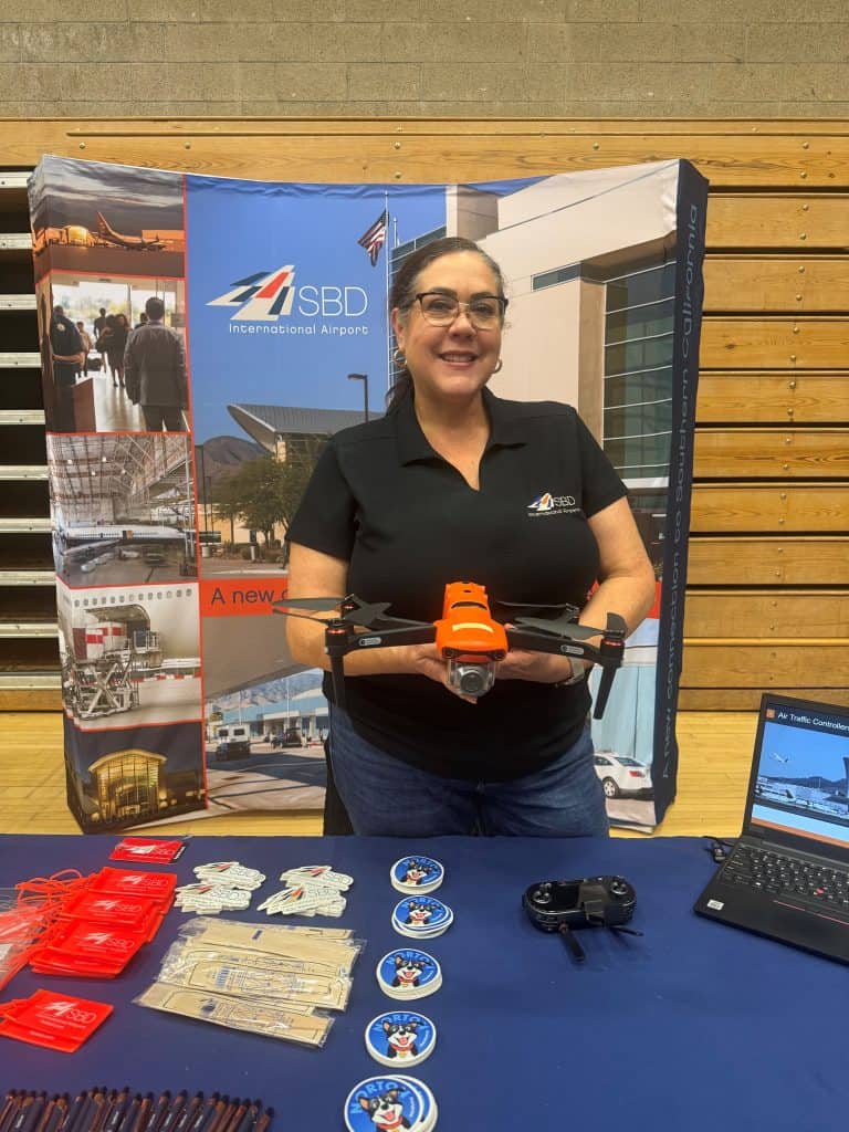 Woman holding a drone behind a table with giveways and a pop up display in the background