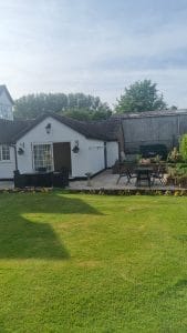 Bright colourful garden with patio and outdoor furniture, home exterior, and lush green lawn.