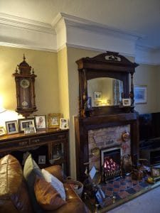 Antique wooden fireplace mantel with mirror in a traditional living room setting.