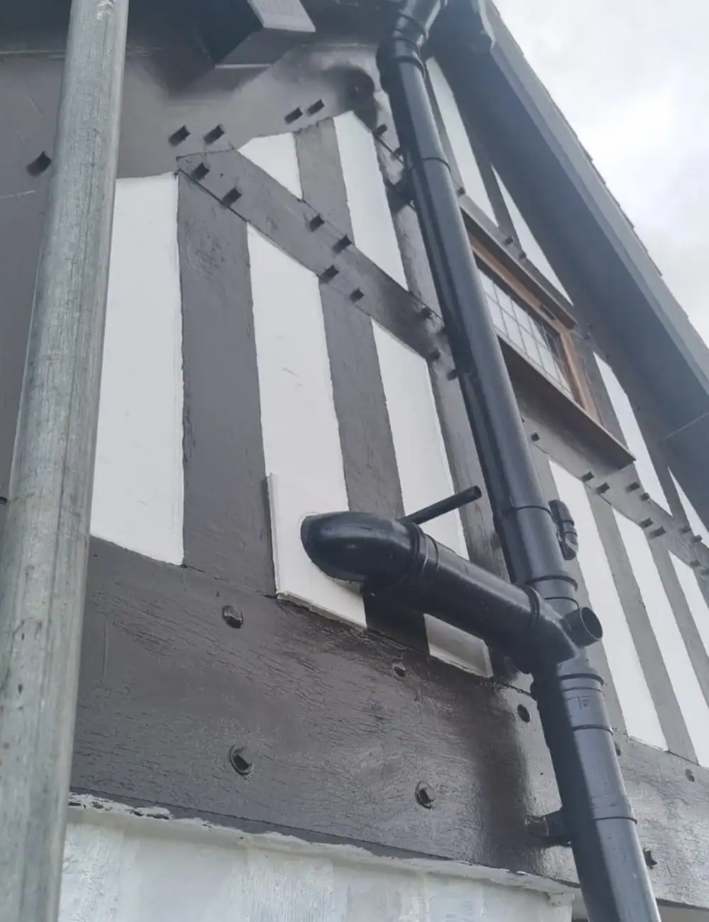 Pipe installation on a traditional black and white Tudor-style exterior wall for renovation.