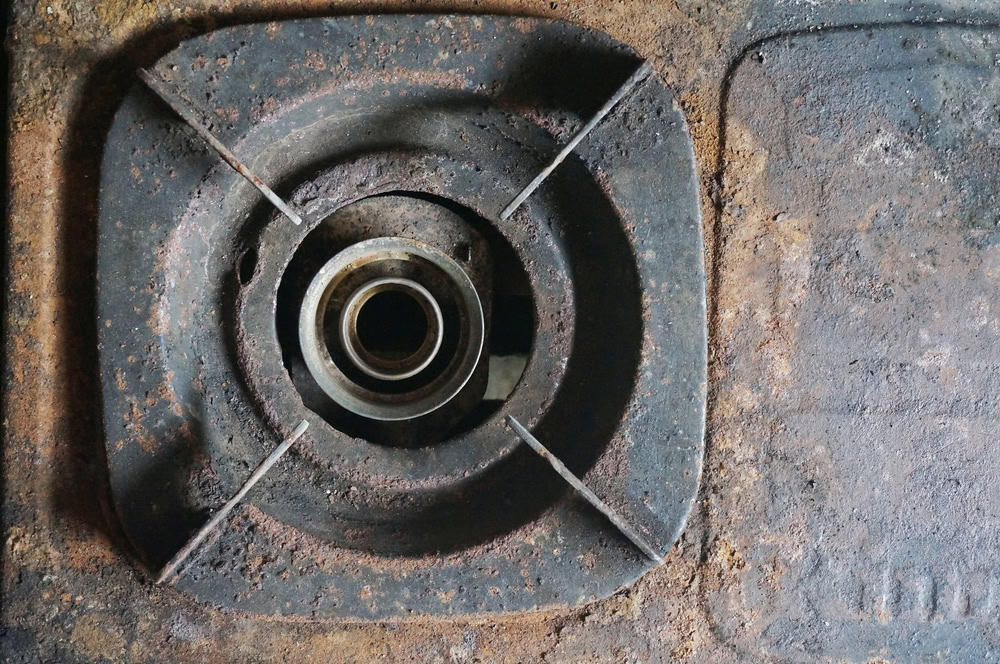 Close-up of a rusty gas stove burner on scrap metal surface.