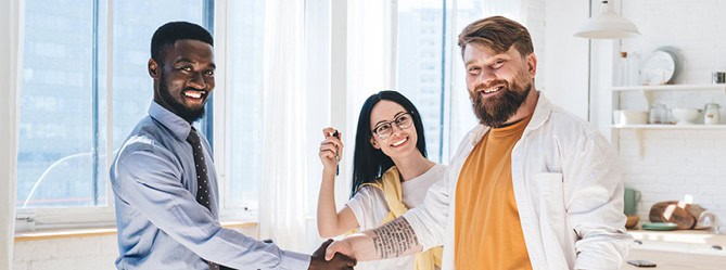 Happy diverse real estate clients shaking hands after property sale, West Michigan home buying and selling success.