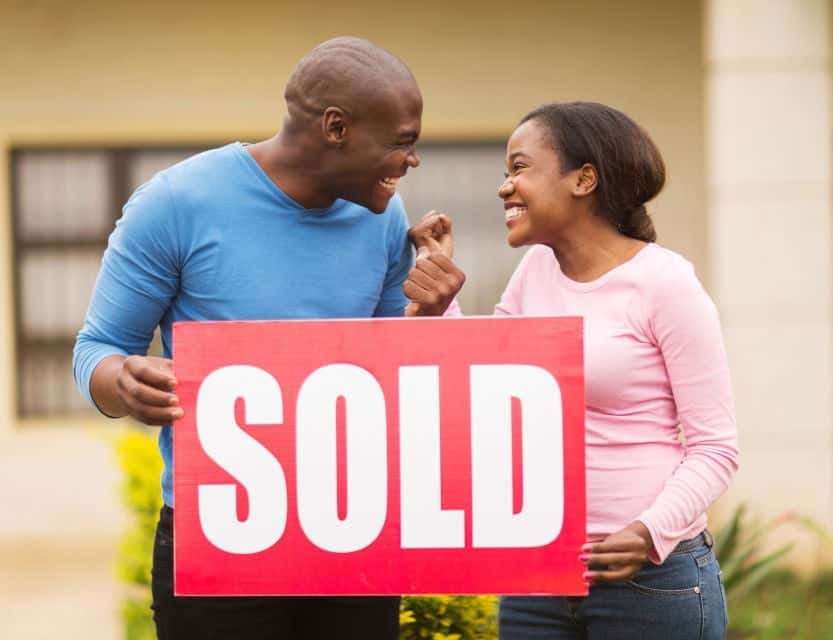 SOLD sign held by happy couple outside a home, celebrating successful house sale in West Michigan.