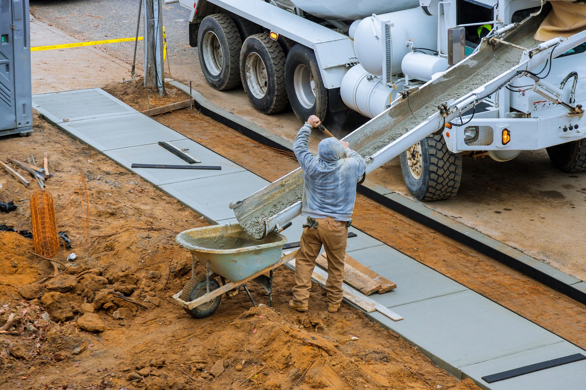Construction worker pour cement for sidewalk in concrete works with mixer truck with wheelbarrow at