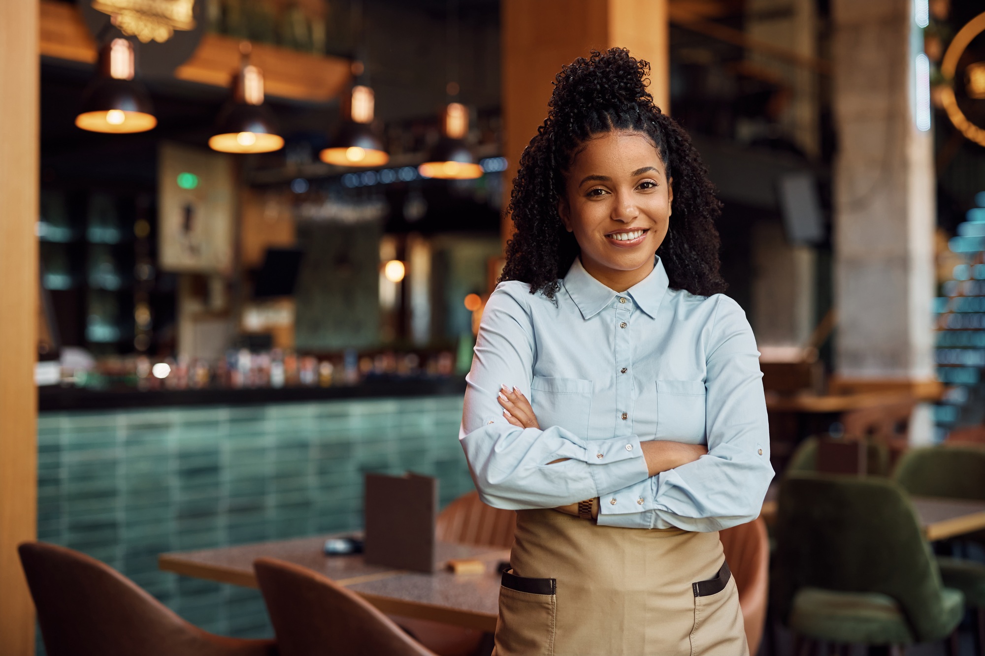 Happy African American waitress with crossed arms in a cafe.,