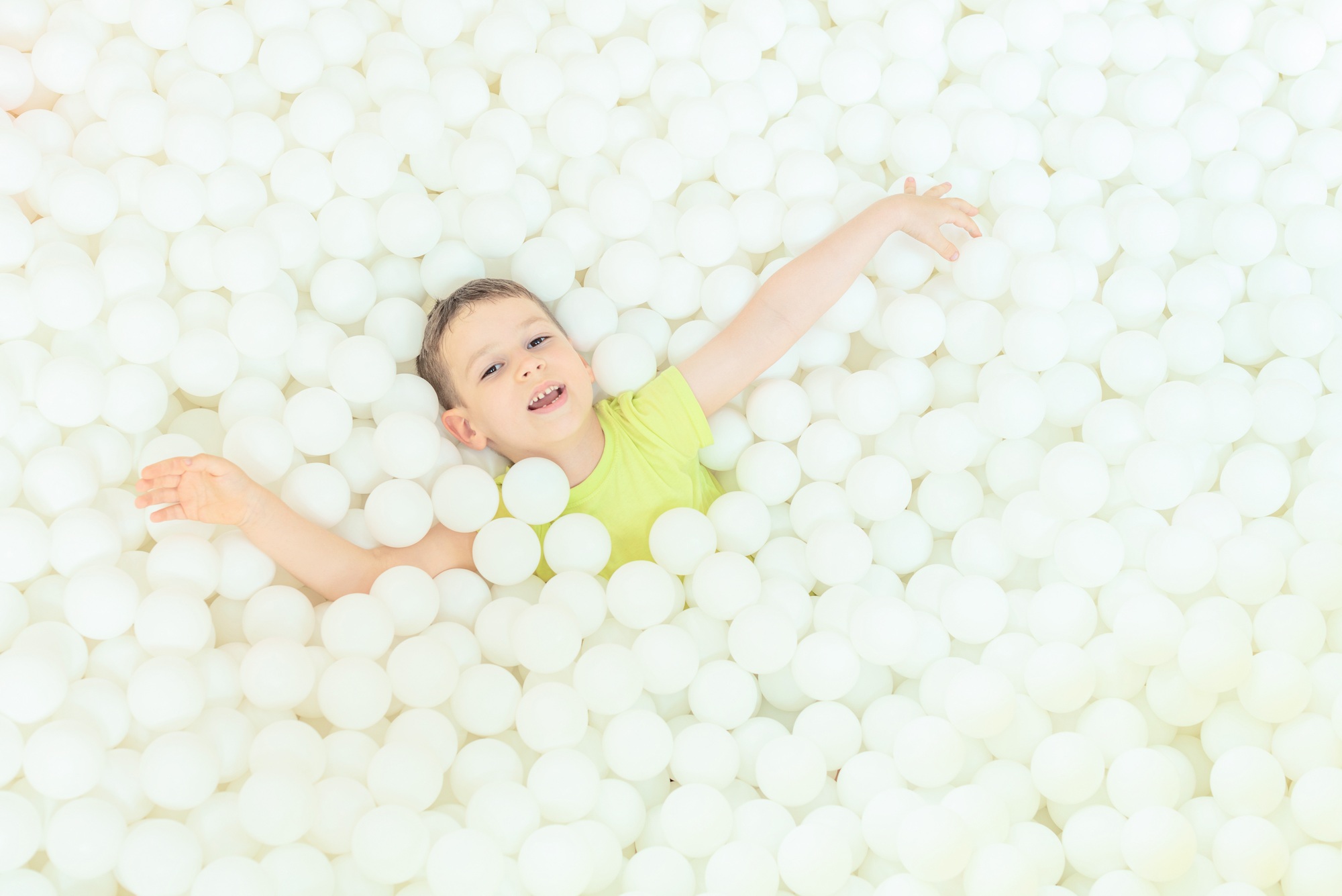 Happy child boy in the big dry pool with thousand of white balls. Childhood concept. Indoor activity