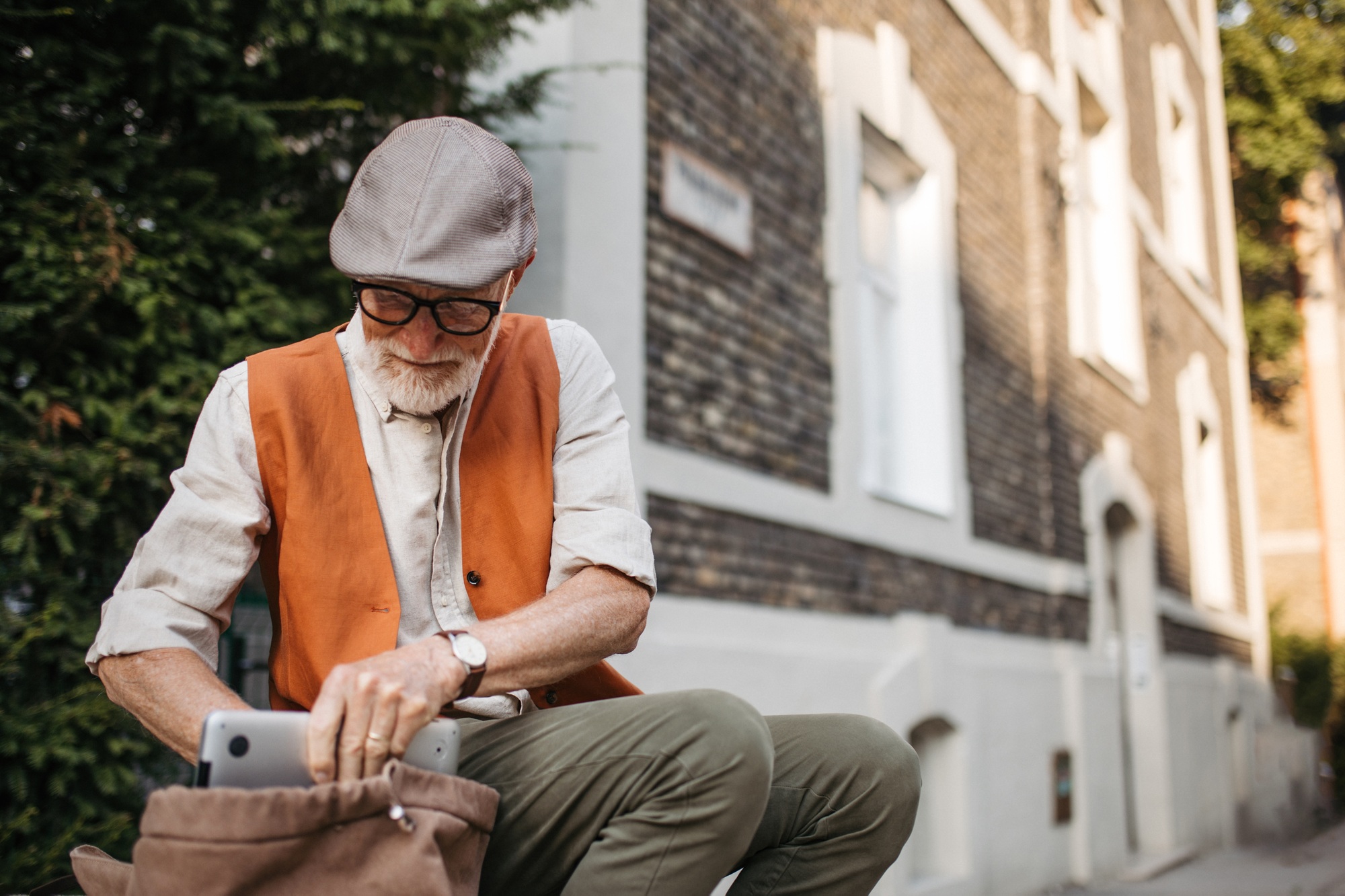 Senior man sitting on street curb in the city. Portrait of elderly man searching for things in a