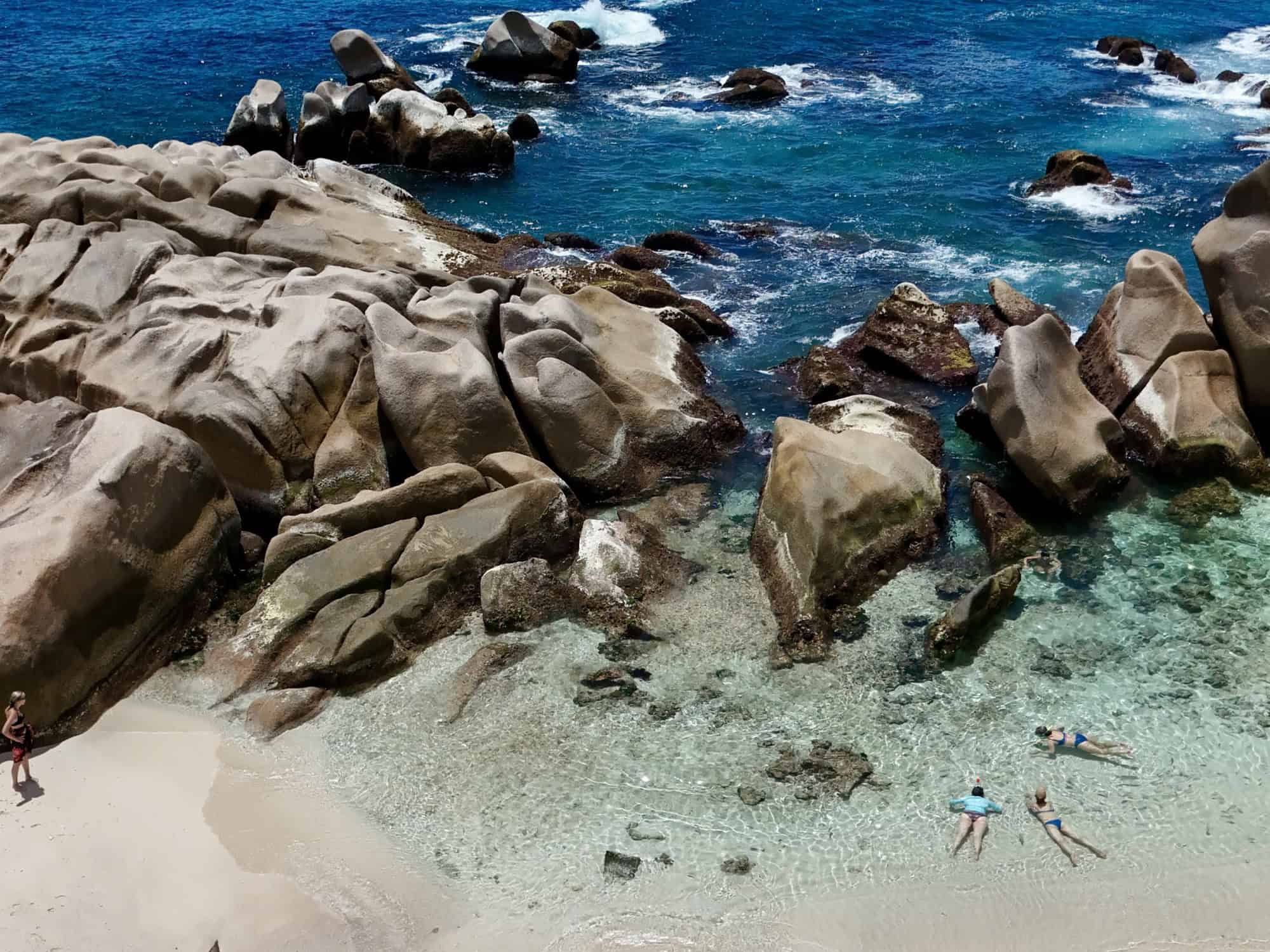 Femme nageant près de rochers sur une plage de sable blanc, mer turquoise, Seychelles, nature, détente, vacances, paysages côtiers, ambiance tropicale, eau claire, roche, plage de rêve, excursion marine, aventure, snorkeling, méditation, paradis insulaire, État insulaire, tourisme nature, beauté côtière, voyage aquatique, exploration marine.