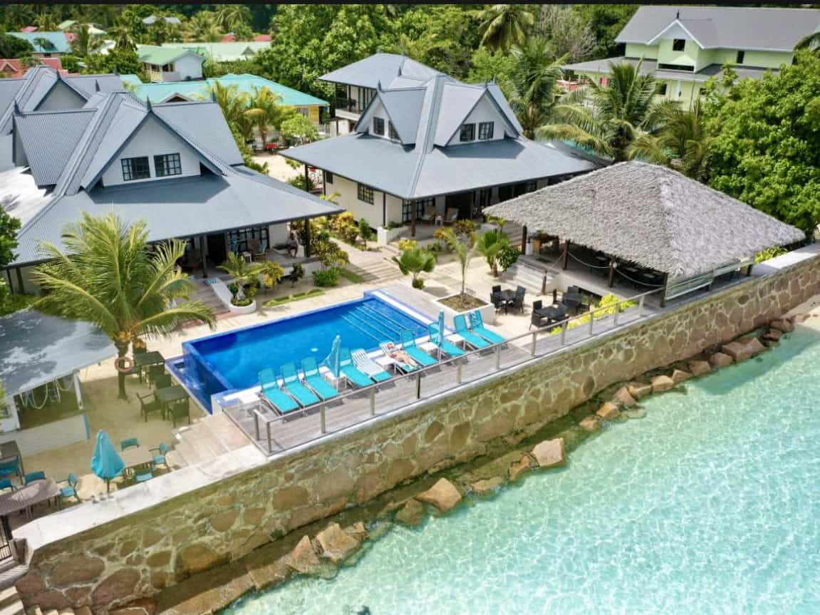 Maisons de vacances avec piscine sur la côte rocheuse de Mahé, Seychelles, entourées de végétation tropicale, avec des chaises longues et un espace détente.