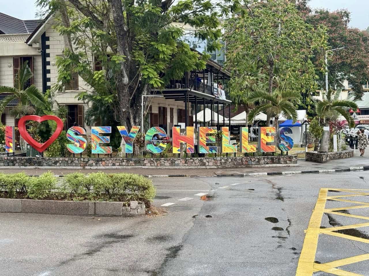 SEYCHELLES sign with colorful letters and a red heart symbol in front of trees and buildings, welcoming visitors to Victoria, Seychelles.