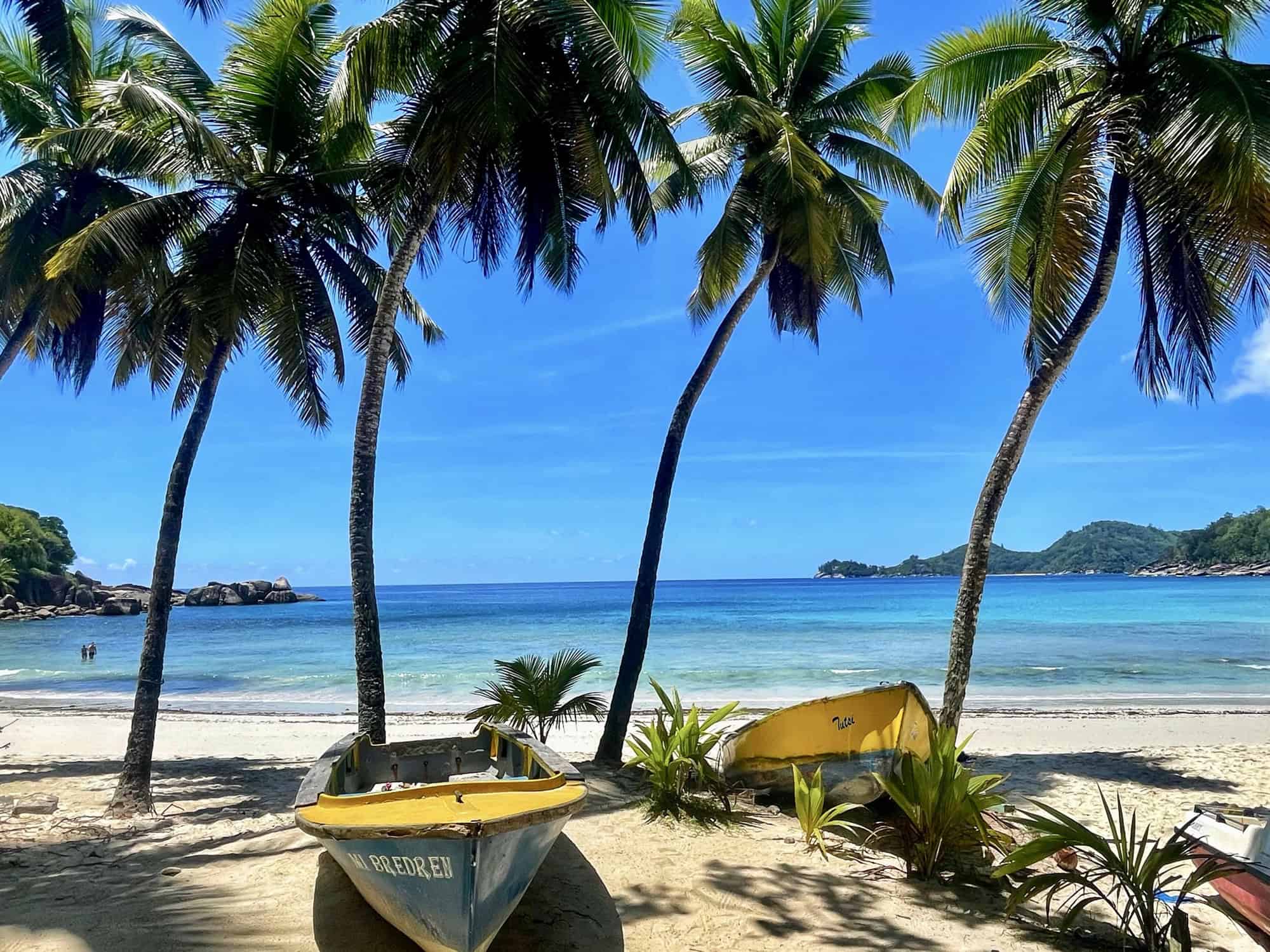 Bateau de pêche sur plage de sable blanc avec palmiers et mer turquoise à Mahé Seychelles.