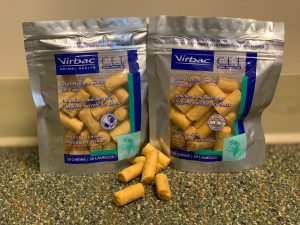Two bags of virbac c.e.t. oral hygiene chews recommended by veterinarians for cats, one with poultry flavor and one for dogs with beef flavor, displayed with sample treats in front on a carpeted floor.