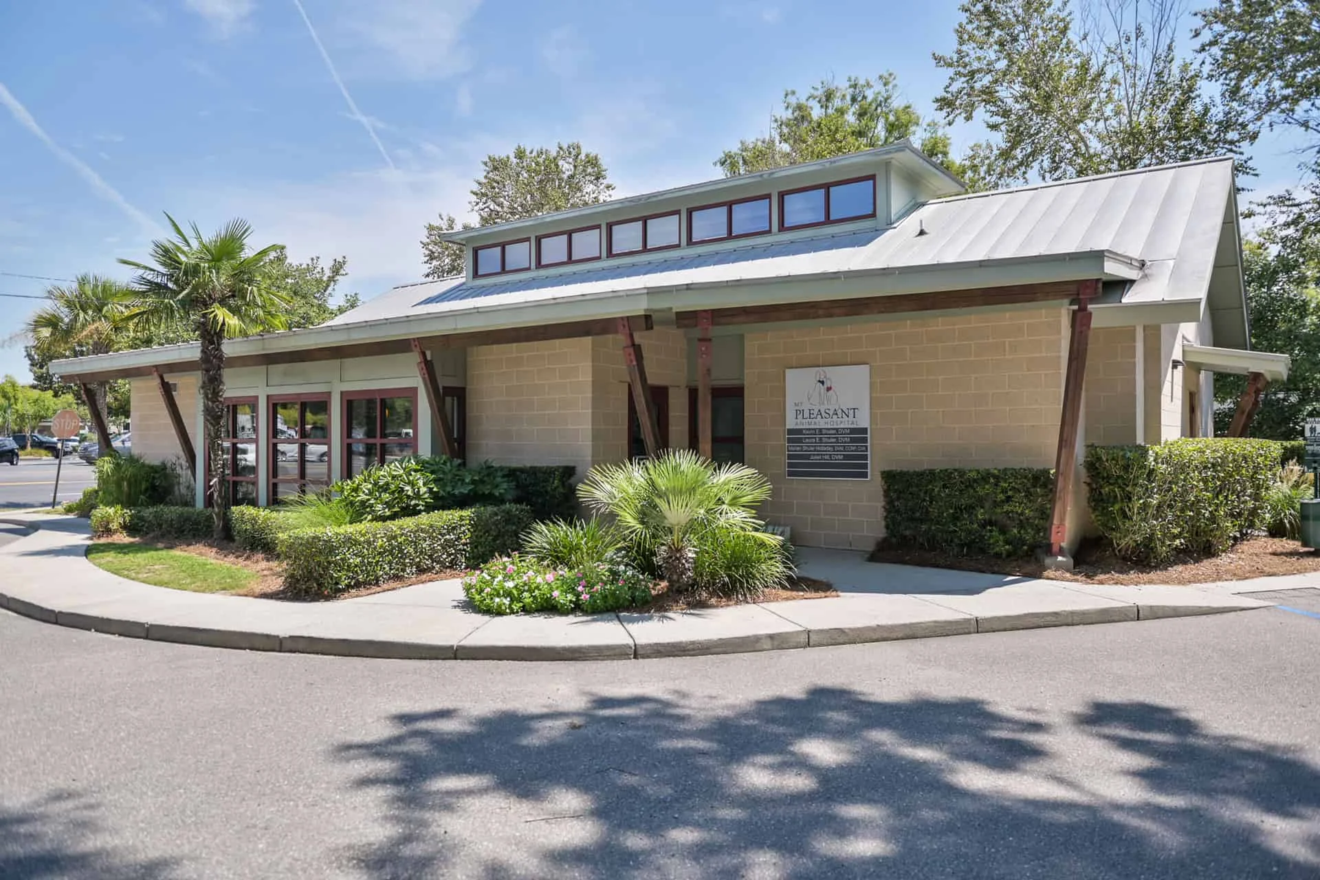 A modern single-story building with a landscaped front yard featuring palm trees and shrubs, under a clear blue sky. A sign by the entrance reads "Pleasant Veterinarian.