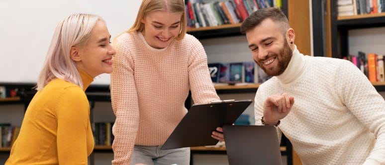 Team of diverse young professionals collaborating with a laptop and tablet in a modern office setting, emphasizing teamwork, digital tools, and workplace productivity.