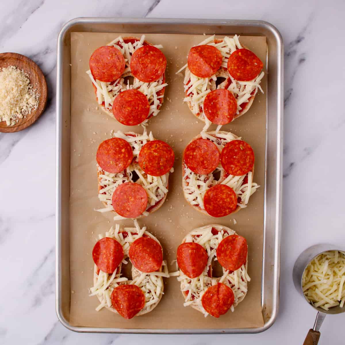 Placing pepperoni slices on top of cheese-covered pizza bagels.