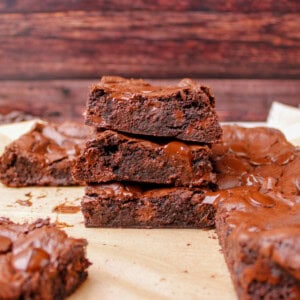 A batch of the best fudge brownies freshly baked in a metal pan with a shiny crinkle top and melted chocolate chips, sliced into squares.