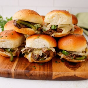 Philly cheesesteak sliders with melted provolone cheese and sautéed peppers served on a wooden cutting board.