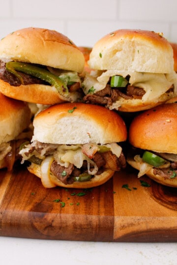 Philly cheesesteak sliders with melted provolone cheese and sautéed peppers served on a wooden cutting board.