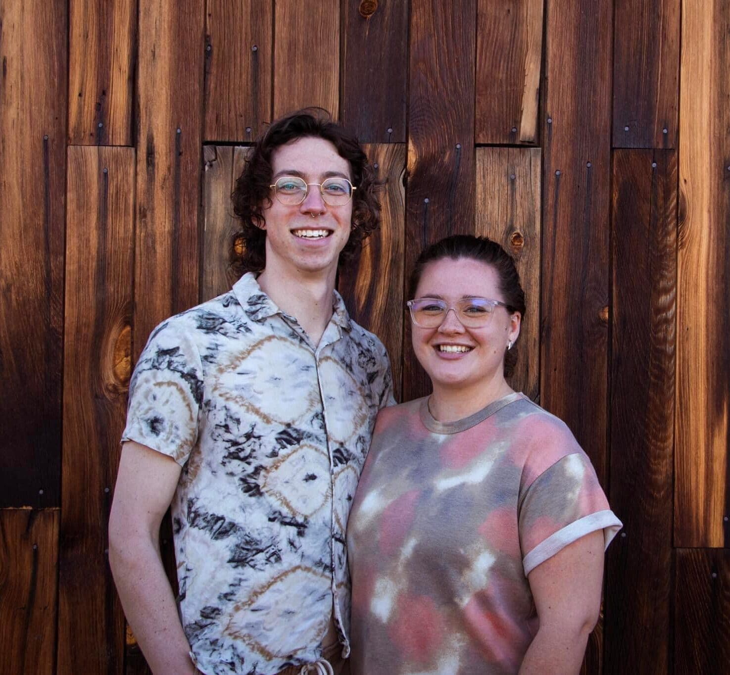 Warm smiling young adults standing in front of a wooden wall, representing singing and ministry.