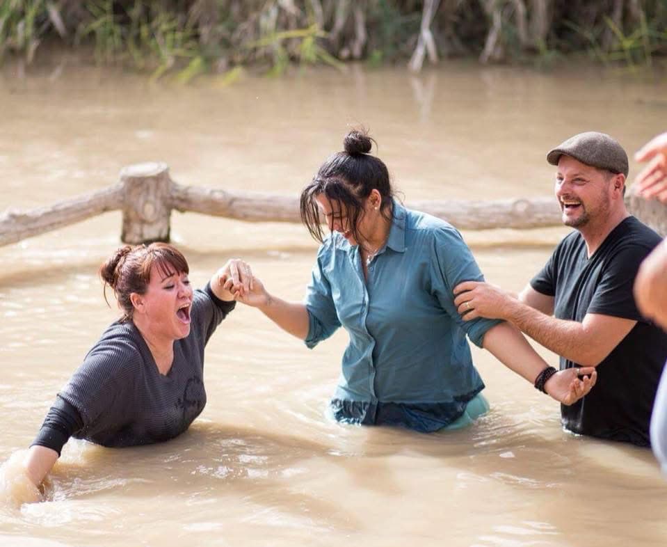Rescue ministry volunteers baptizing a woman in muddy water during a faith event.