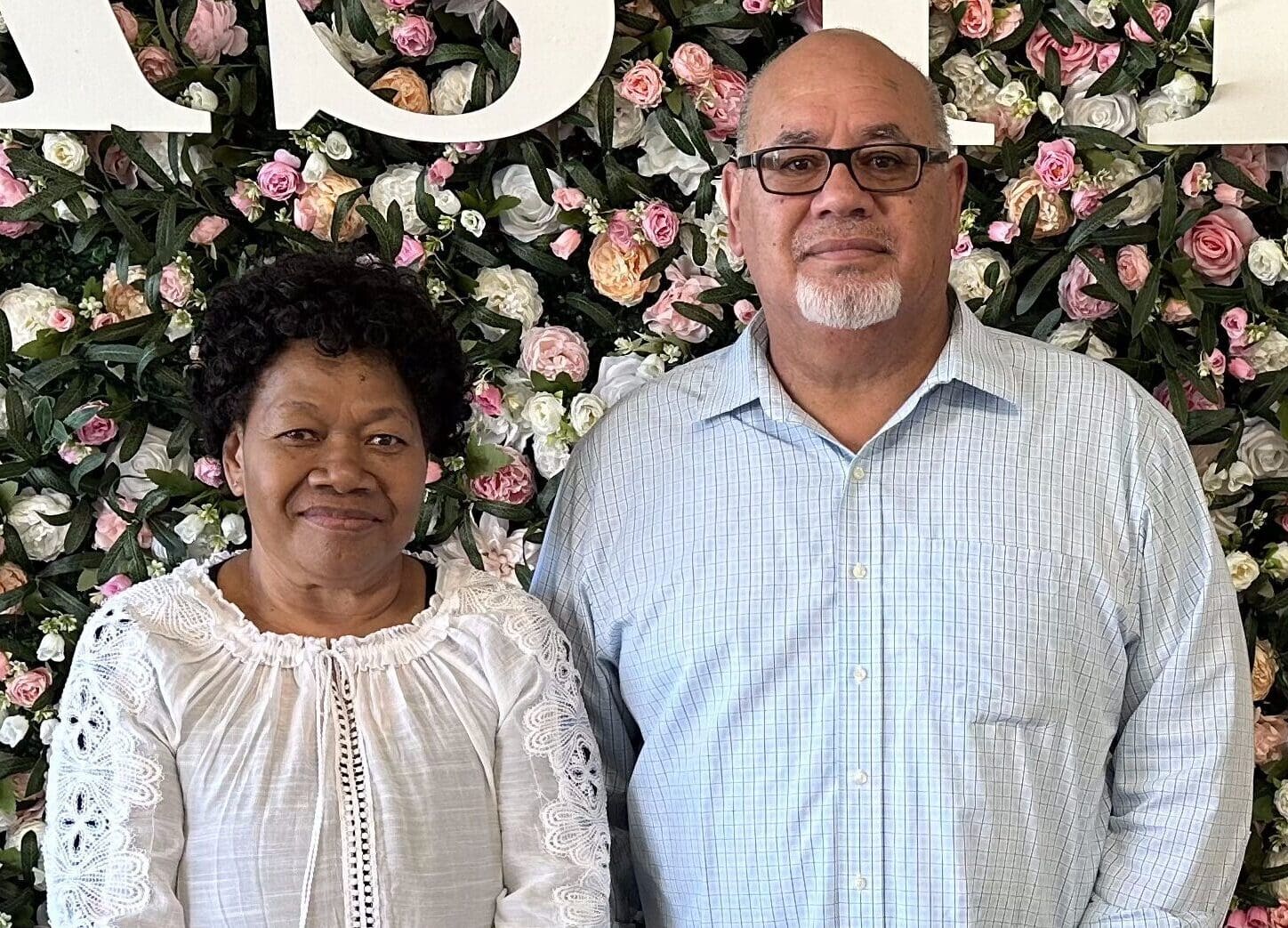 Senior couple standing with floral background at Singing Feather Ministries event, promoting faith and community.