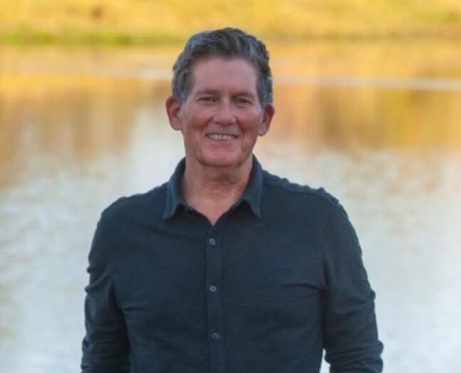 John smiling outdoors by a lake, promoting faith-based community services and Christian ministry outreach.