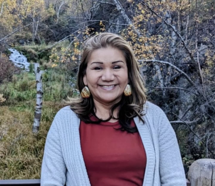 Joyful woman smiling outdoors at Singing Feather Ministries, surrounded by nature and autumn foliage.