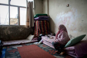 Refugee woman praying indoors, seeking hope and comfort, Bible and prayer in focus, promoting faith-based support.