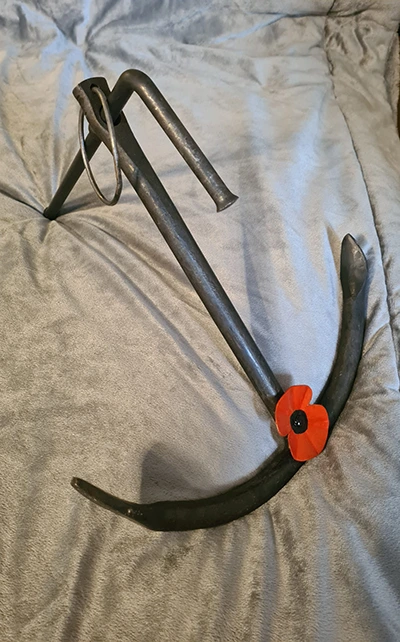 Metal anchor with red poppy on gray fabric.
