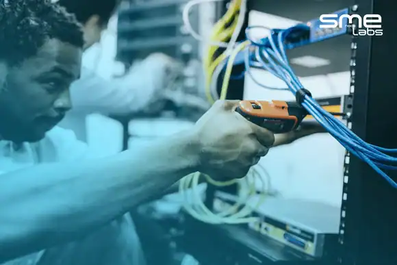 Technician testing network cables in a server room with a cable tester.