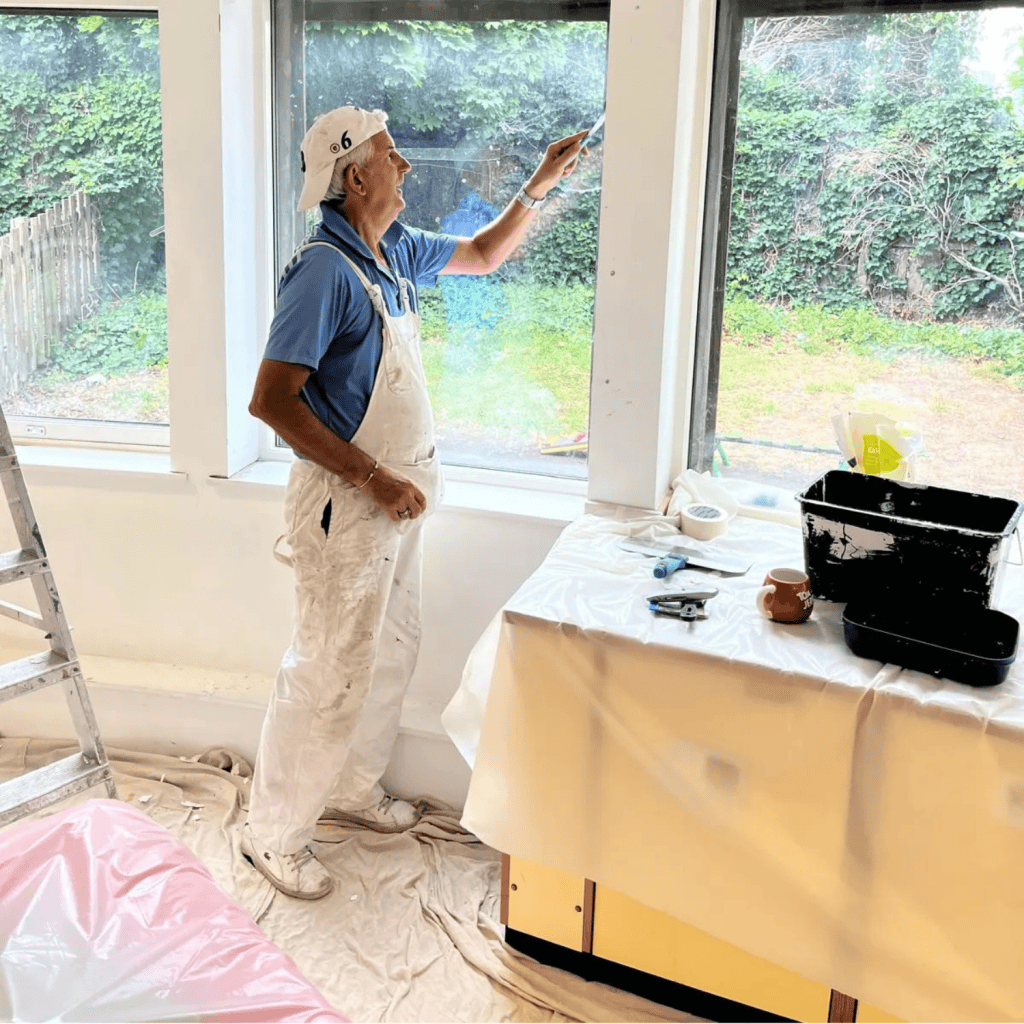 Painter decorating interior wall near large windows