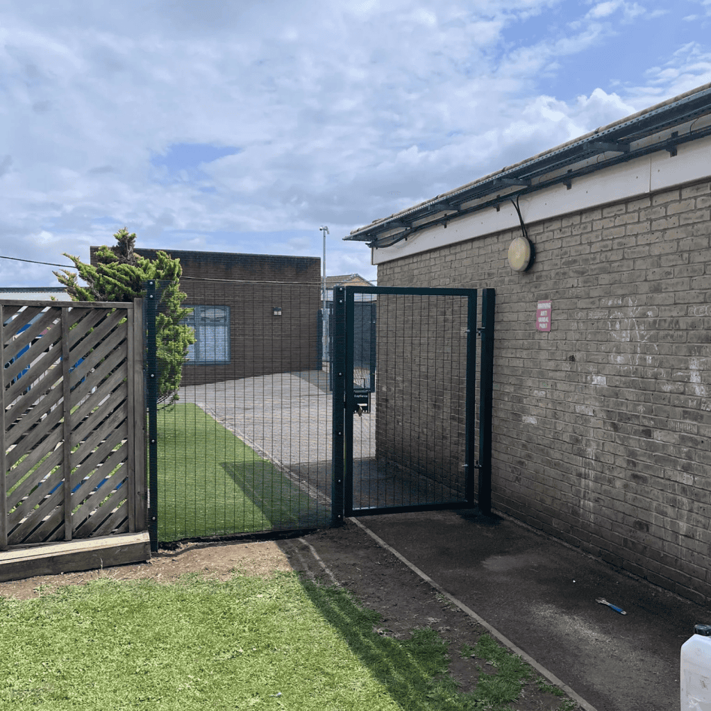 Green metal gate and fence installation next to brick building