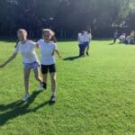 two pupils running in a sunny field wearing gym wear