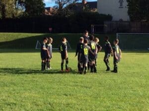football players standing in a circle being spoken to by the coach
