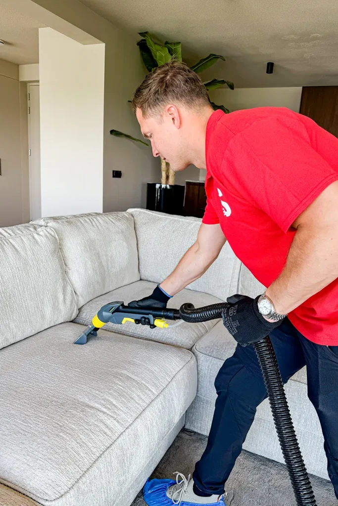 Professionele reiniger stofzuigt bank voor een schone woonkamer.