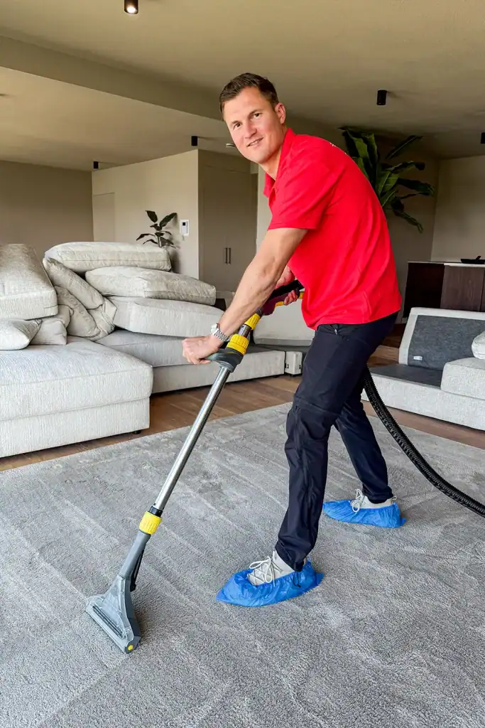 Man reinigt tapijt met professionele stofzuiger in woonkamer.