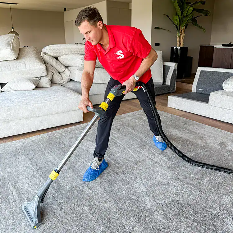 Man reinigt tapijt met professionele stofzuiger in woonkamer.