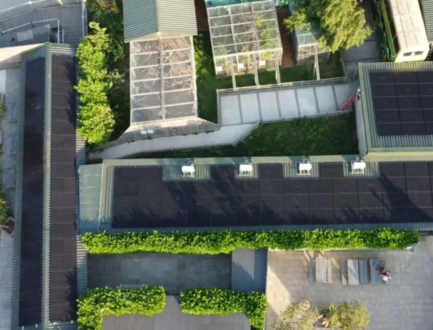 Aerial view of solar-powered greenhouses and rooftops equipped with solar panels, showcasing sustainable energy solutions for gardening and commercial use.