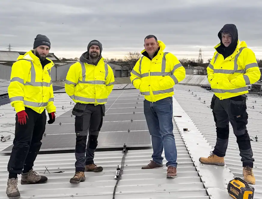High-visibility solar panel installation team on roof with solar panels, wearing yellow safety jackets.