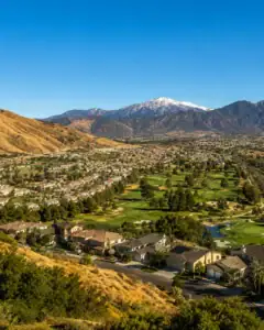 Beautiful landscape of Yucaipa, California, featuring a golf course, residential area, and snow-capped mountains in the background under a clear blue sky.